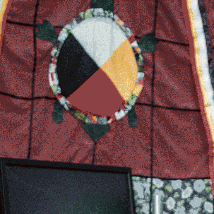 Quilt with a Medicine Wheel in the middle hanging on a wall in First Nations House.