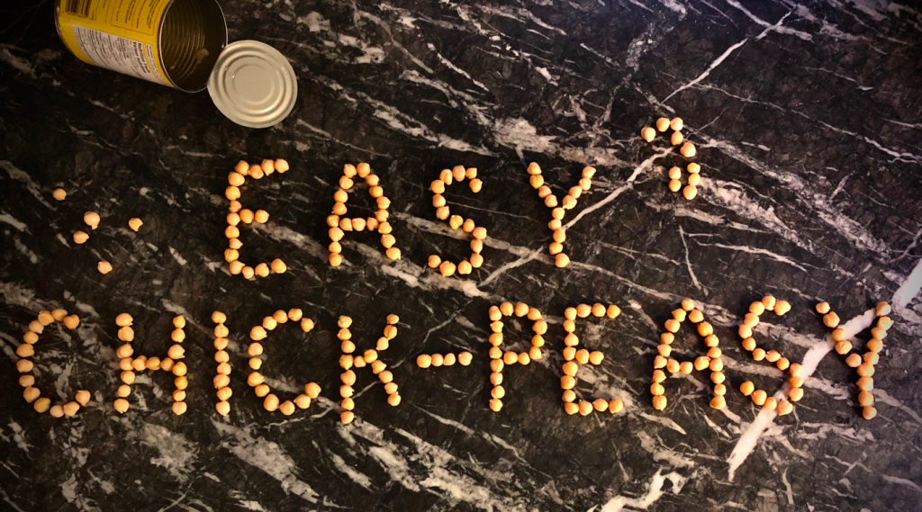 the words "Easy Chick-Peasy" are spelt out in chickpeas across a kitchen counter top. 