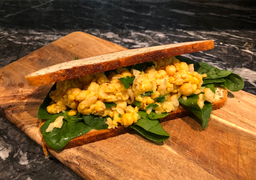 Image of chickpea salad in a sandwich with spinach on a cutting board