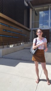 Tamsyn stands in front of the steps at the Monk School of Global Affairs. News headline tickers can be seen in the background.