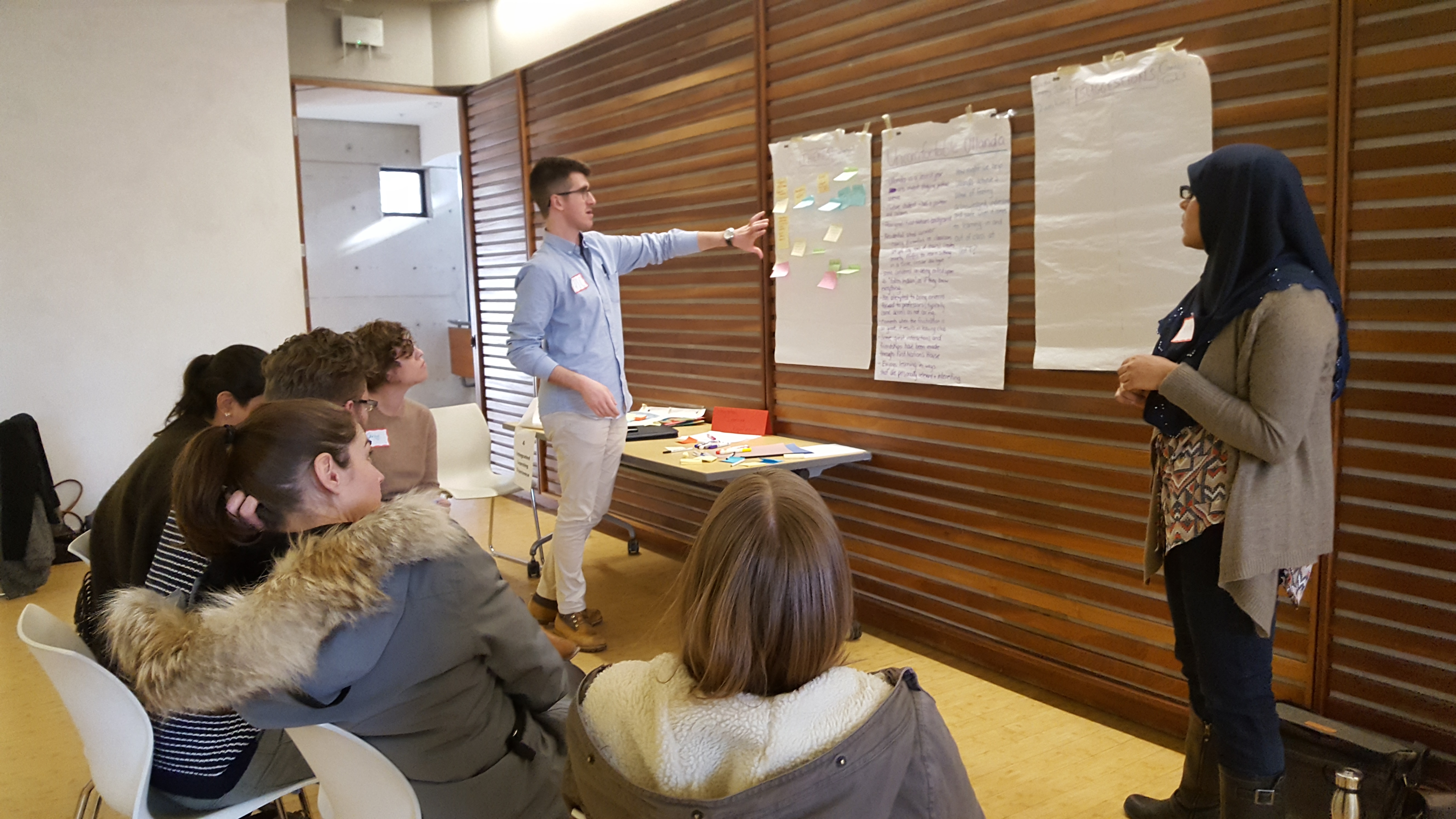 Individuals surround paper posted to a wall, discussing ideas and writing down concepts.