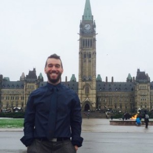 Smiling young man in blue dress shirt and tie in front of Parliament Hill 
