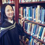 Photo of Dr. Meng Xiao in a library, looking to the camera and smiling