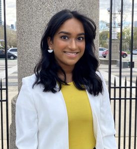 Shankeri is standing outside, wearing a yellow top with a white blazer.