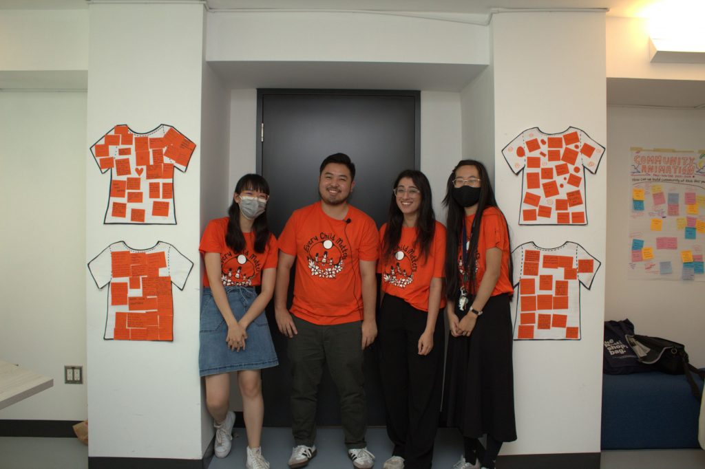 Four students standing in front of a door surrounded by the Orange Shirt Day mural.