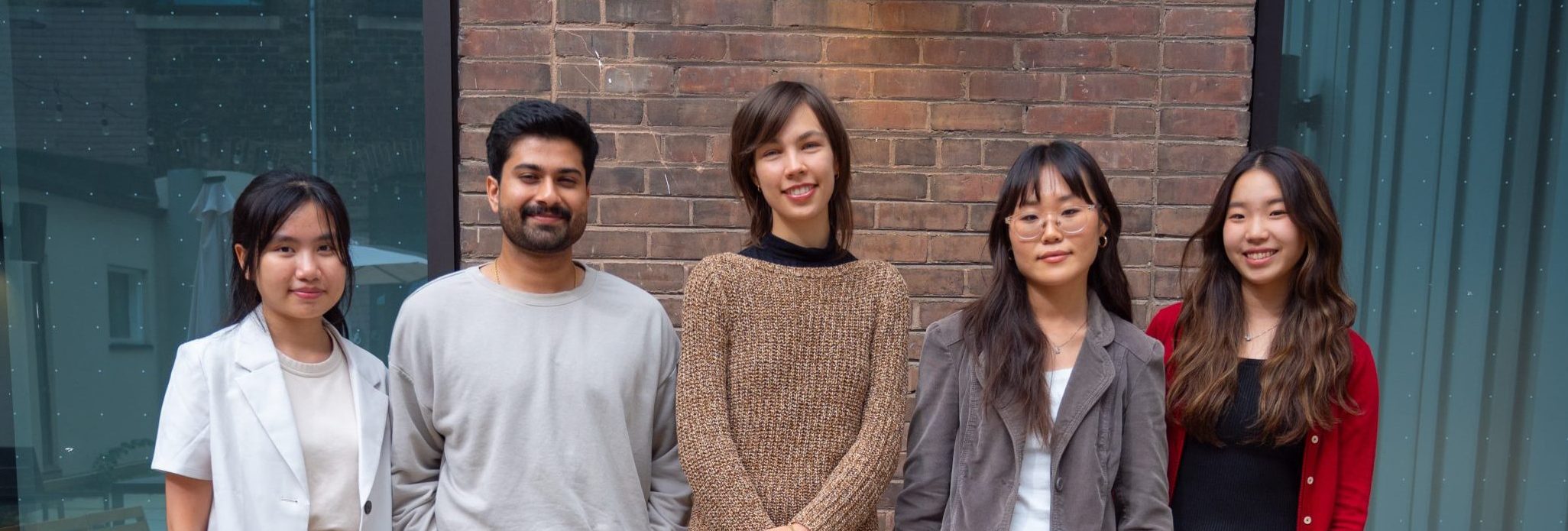 A photo of the Audiovisual Storytelling team, featuring five team members standing outdoors against a brick wall, smiling at the camera.