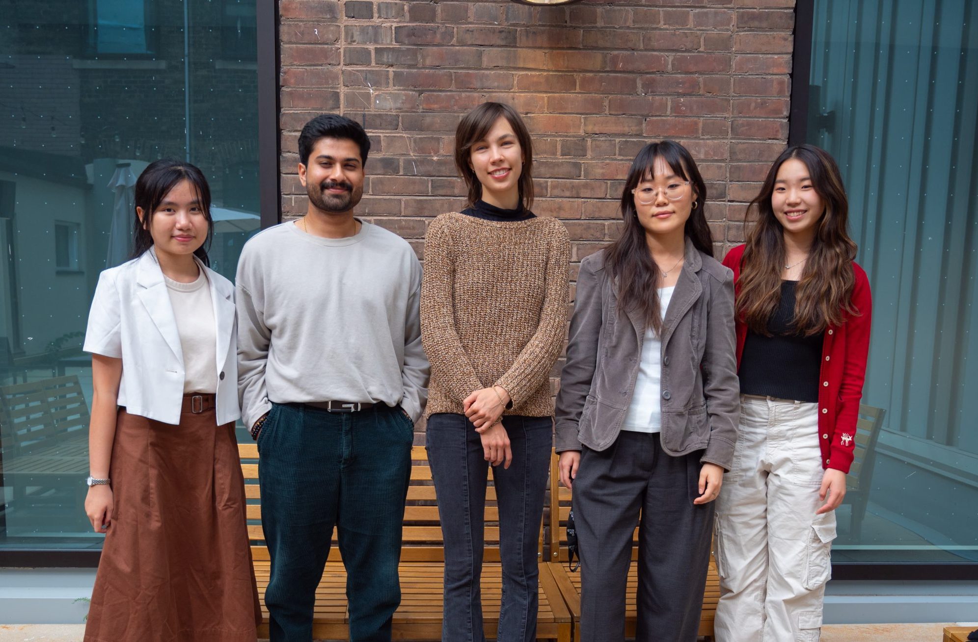 A photo of the Audiovisual Storytelling team, featuring five team members standing outdoors against a brick wall, smiling at the camera.