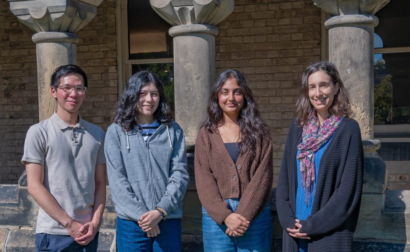 A photo of the Blog Editors & Content Writers team, featuring four members standing outdoors in front of a brick building with stone columns, smiling at the camera.