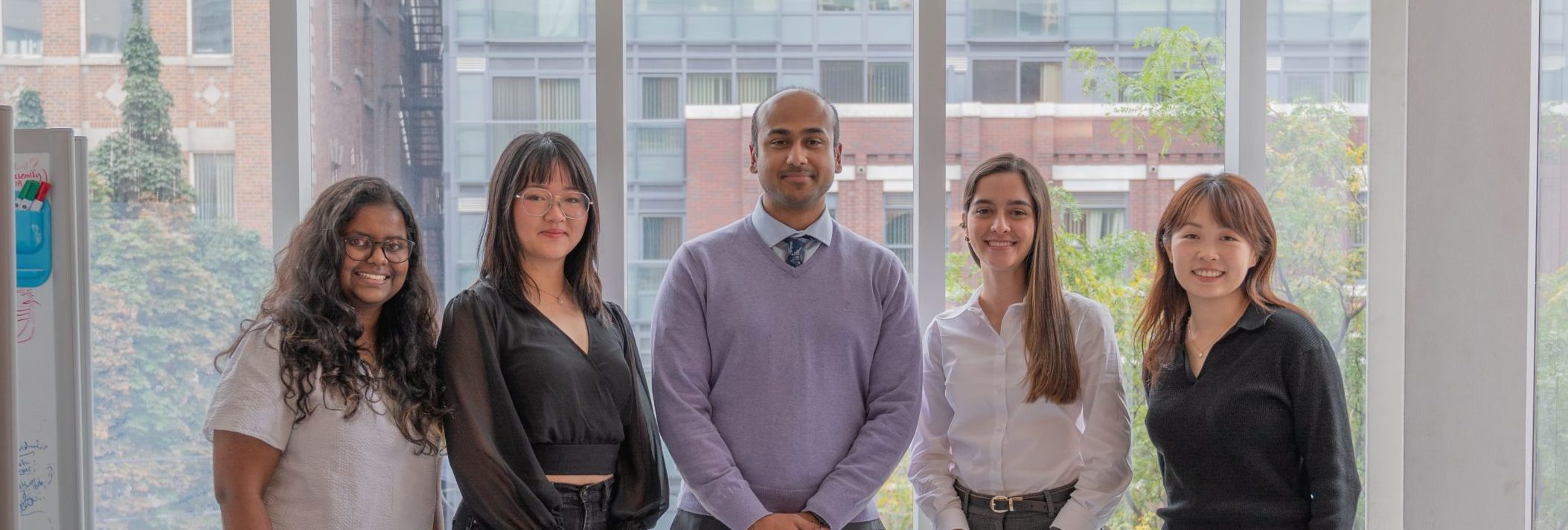 A photo of the "EDIA at School of the Environment" team, featuring five members standing indoors in front of large windows, smiling at the camera.