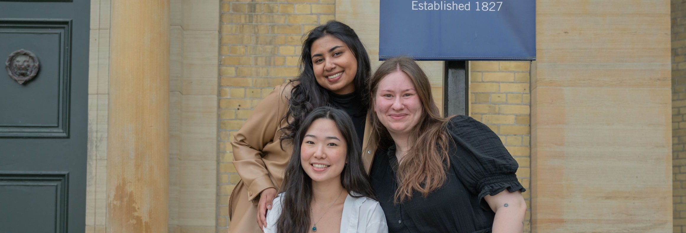 A photo of the Process Guides team, featuring three members standing outdoors in front of a building, smiling at the camera