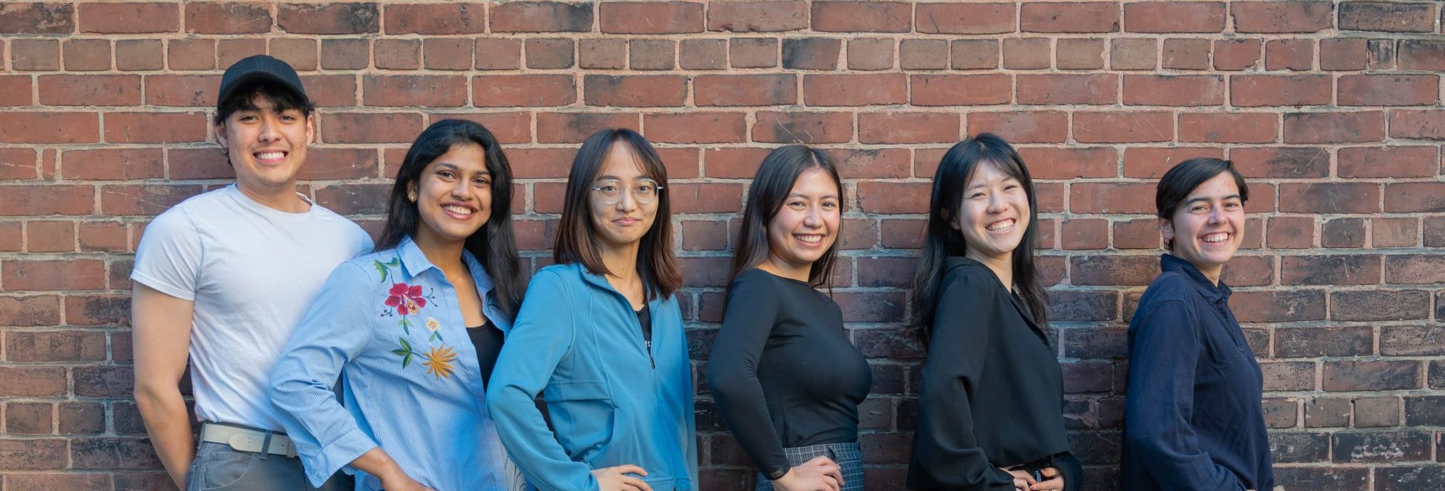 The photo of the UXUI Web Design Team features 6 people sitting in front of a brick wall and smiling.