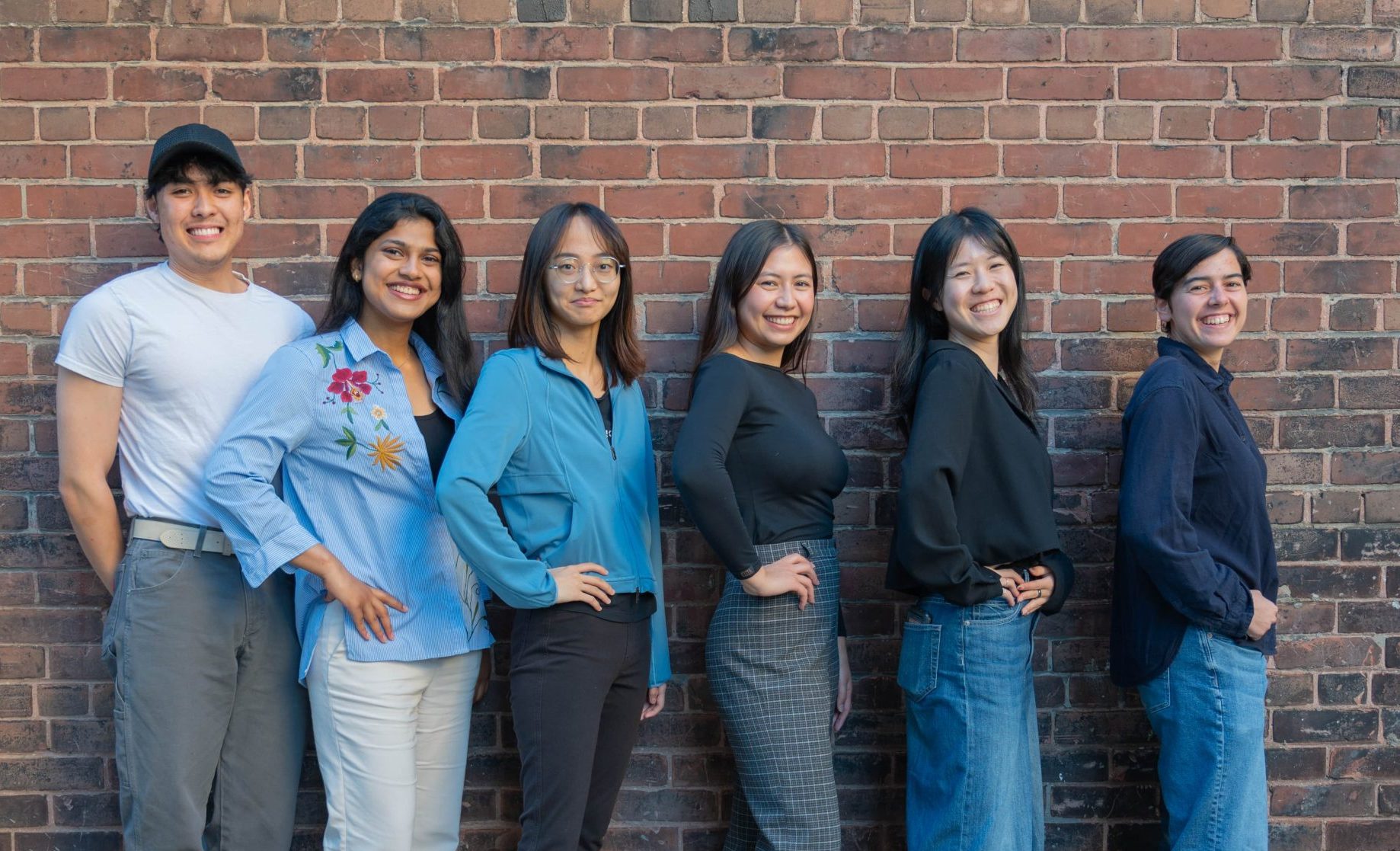 The photo of the UXUI Web Design Team features 6 people sitting in front of a brick wall and smiling.