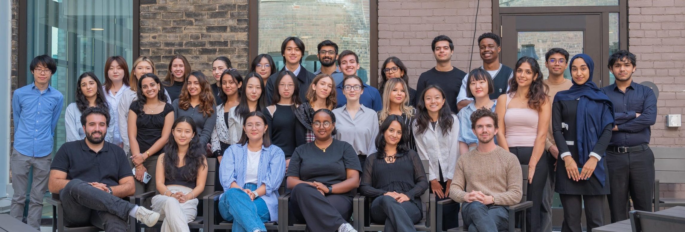 A group photo of the "A&S University of Toronto Quality Assurance Process (UTQAP)" team, featuring over 30 members standing and sitting outdoors in front of a brick building, smiling at the camera.