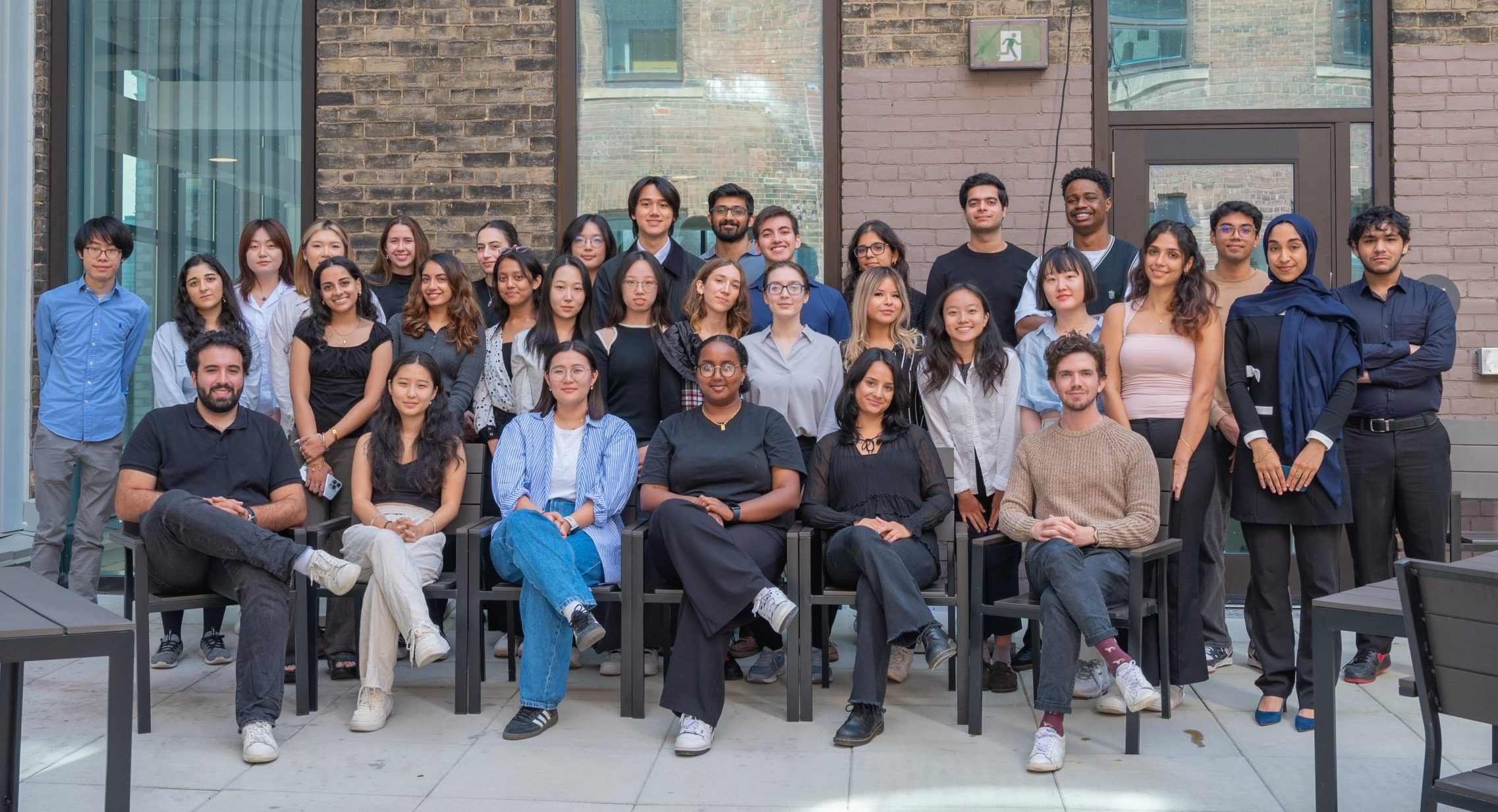 A group photo of the "A&S University of Toronto Quality Assurance Process (UTQAP)" team, featuring over 30 members standing and sitting outdoors in front of a brick building, smiling at the camera.