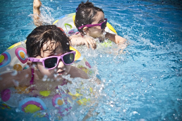 Two small children in pink wayfarer sunglasses swimming in pool floaties