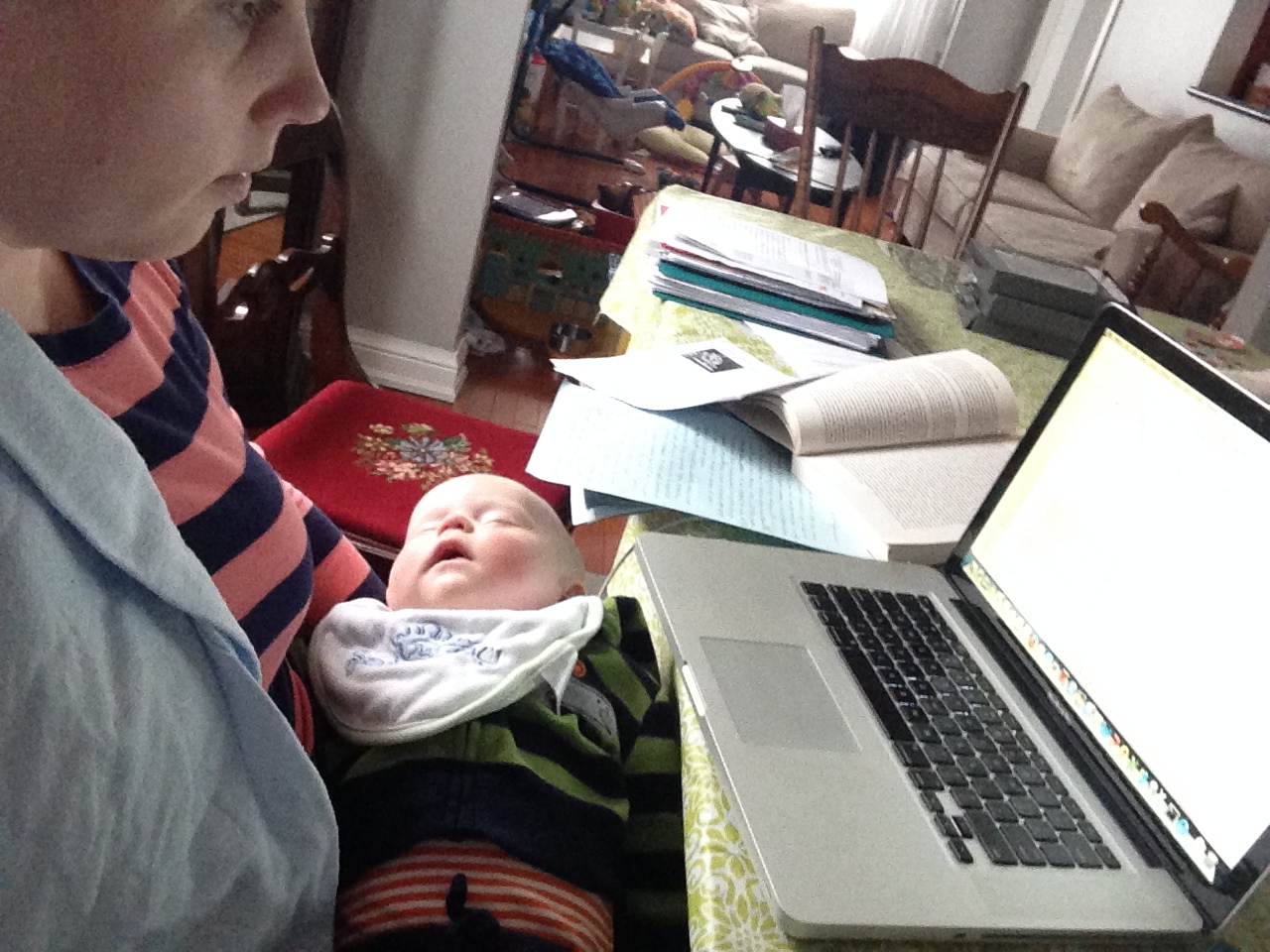 Parent holding baby and studying on laptop.