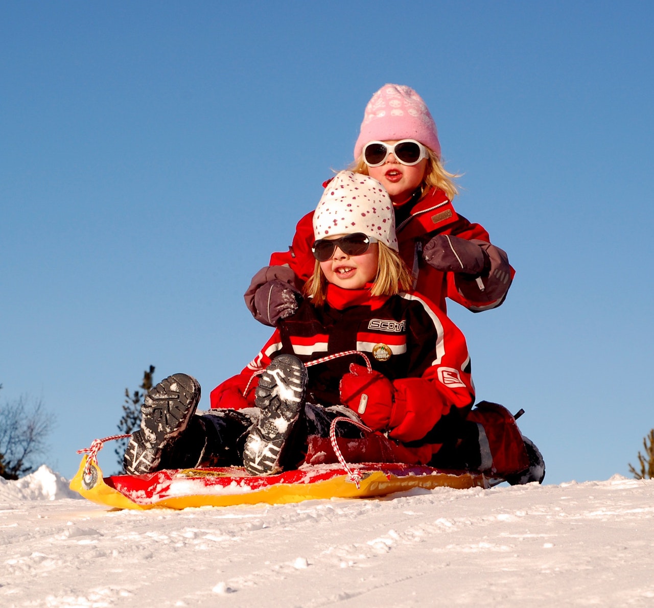 Two girls in red jackets sitting on a sled in the snow.