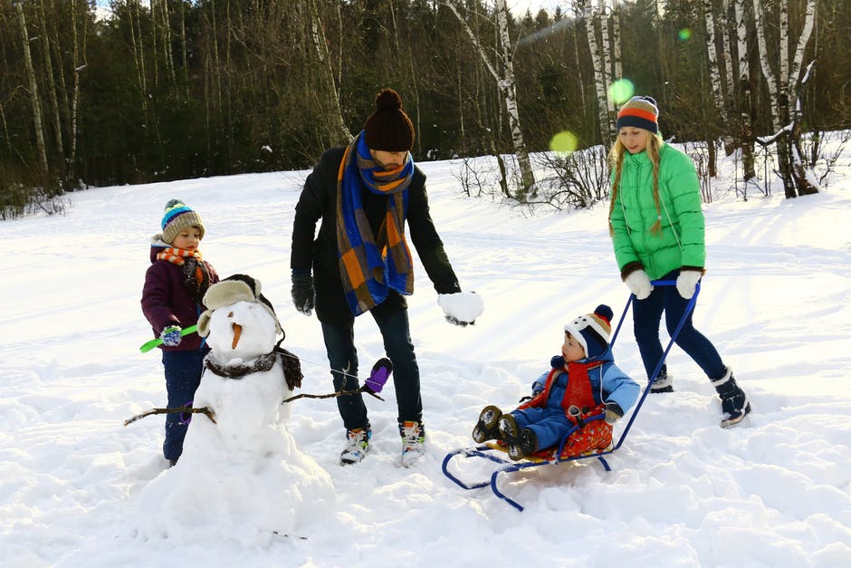Family of four standing on an ice rink in the winter, building a snowman.