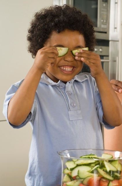 A child holding up sliced cucumbers over his eyes.