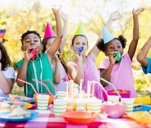 Six children sitting at a picnic table with brighly coloured birthday hats.