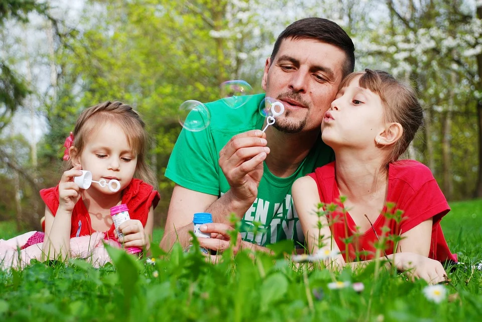 An adult and two children laying on the grass blowing bubbles