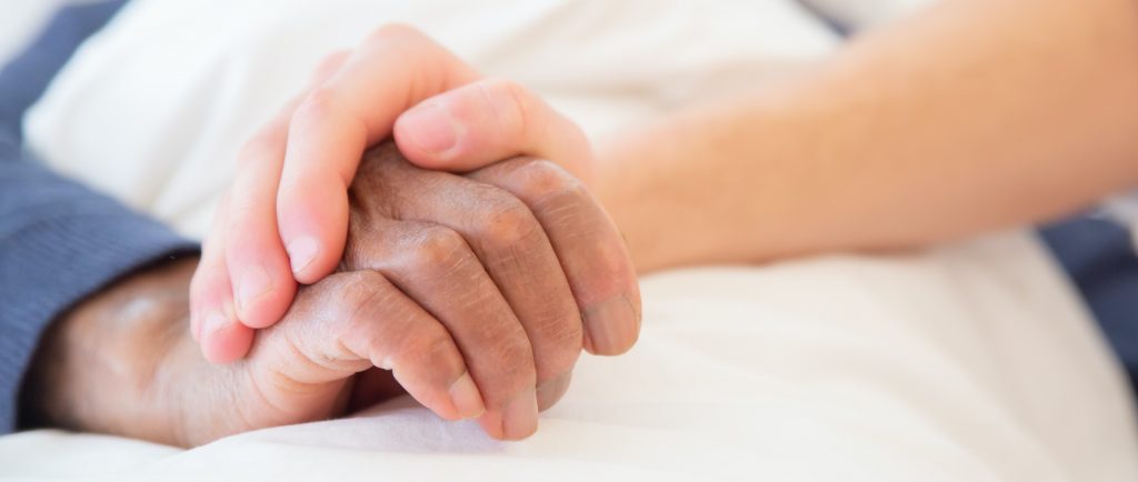 Person in bed with their hand being held by another person