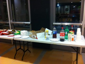A table with pop, chips, a cake, and some tim hortons donuts. 