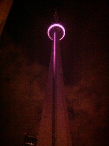 Looking up at the CN Tower from it's base in the dark of night, with the tower lit in pink and all the fog around it pink as well