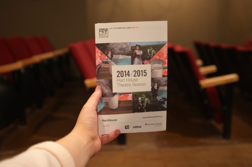 a hand holding out the programme for the 2014-2015 hart house theatre season