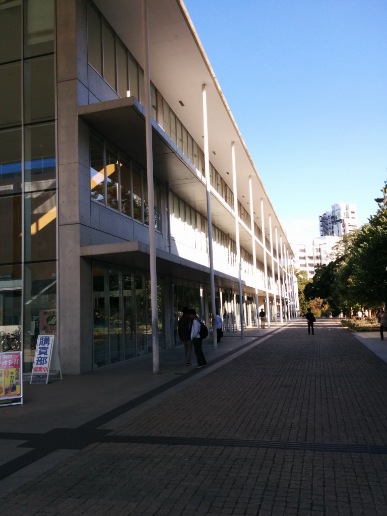 This image shows a paved corridor at the University of Tokyo's Komaba Campus. There is a concrete building to the left of the corridor.
