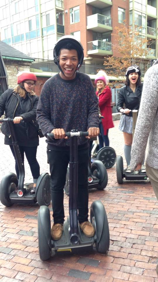 Me smiling while tightly gripping on to the handle bars of the Segway. Behind me are a few of my friends trying to photobomb the shot!