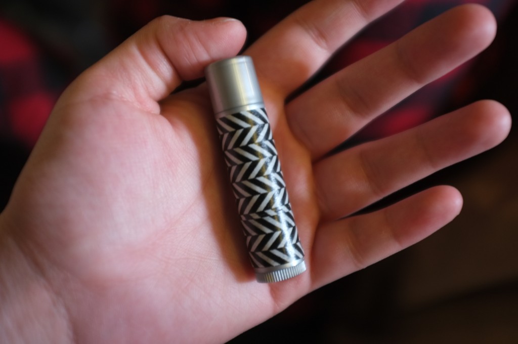 a hand holding a tube of lip balm in the palm. The tube has a geometric pattern on it from washi tape that has been applied to it. 