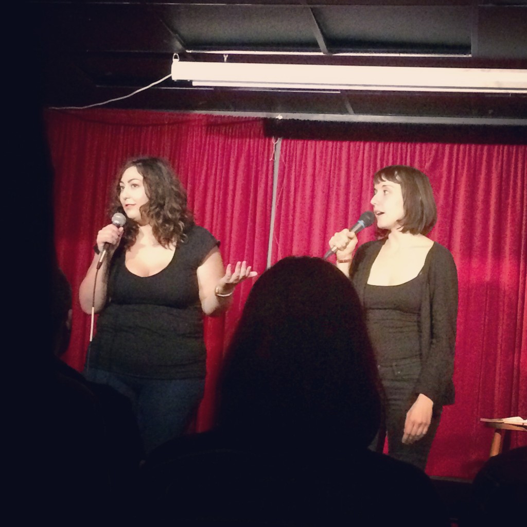 Natalie and Jess (AKA Crimson Wave) performing their opening monologue in front of a red velvet curtain stage.