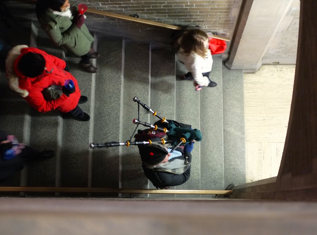 view from above: a bag piper descends stairs with other people behind him 