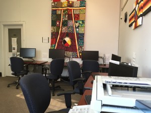 A view over a photocopier, looking towards a row of computers with a large colourful mural in Native styling as the background