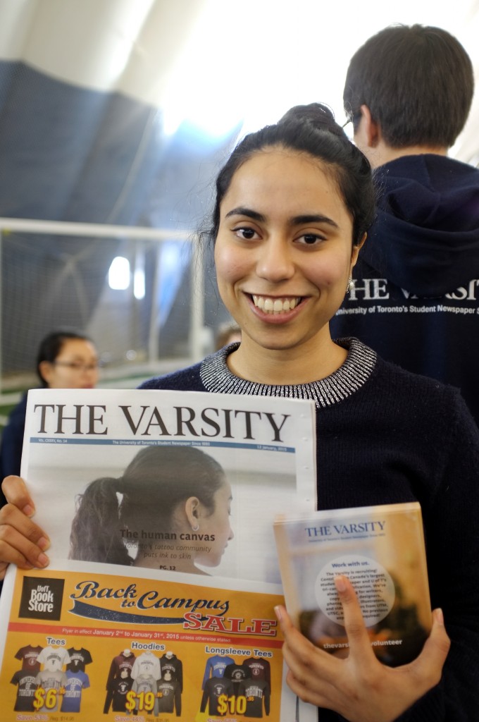 a girl smiles for the camera holding a copy of the varsity magazine up in front of her chest