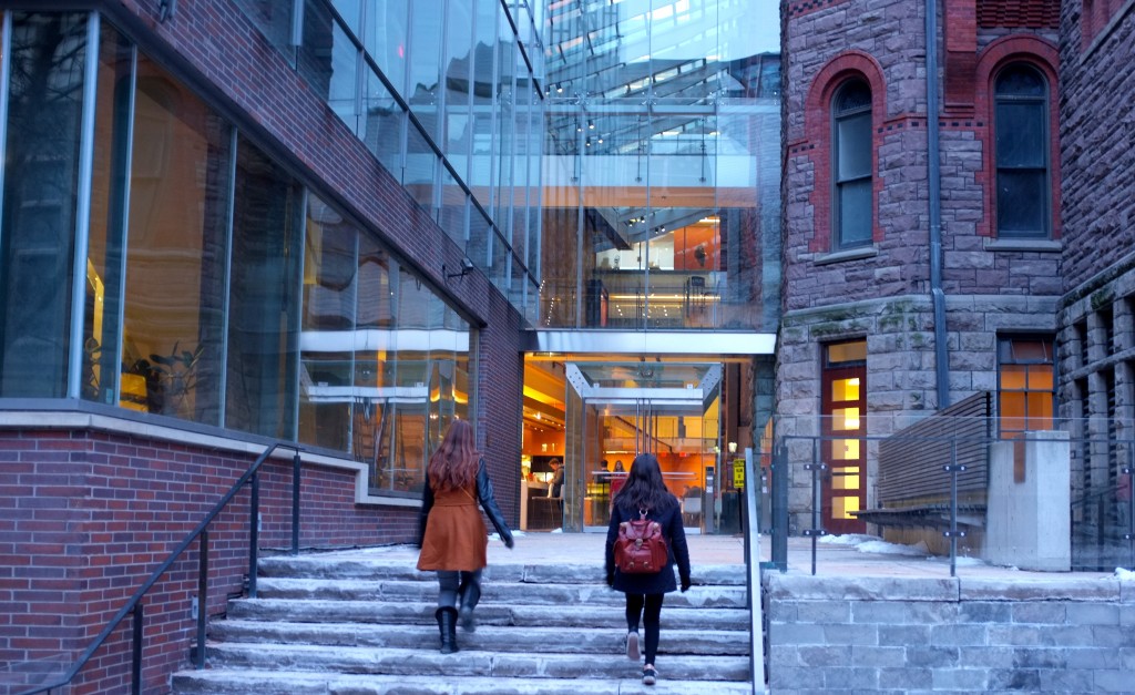 two people walk up steps towards a glass entranceway between two old buildings