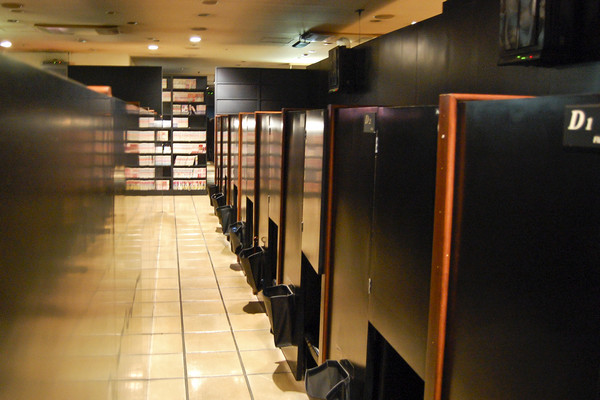 This image shows a row of booths inside a net cafe. Volumes of manga can be seen in a wallshelf in the background.