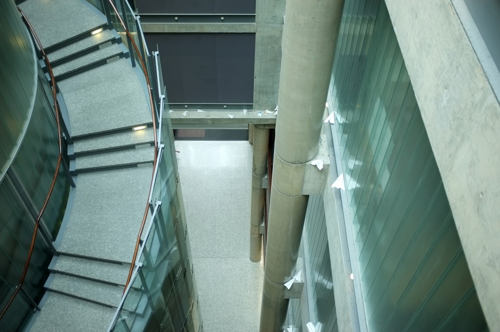 looking down at a curved staircase, there are lots of paper airplanes on a ledge near the staircase
