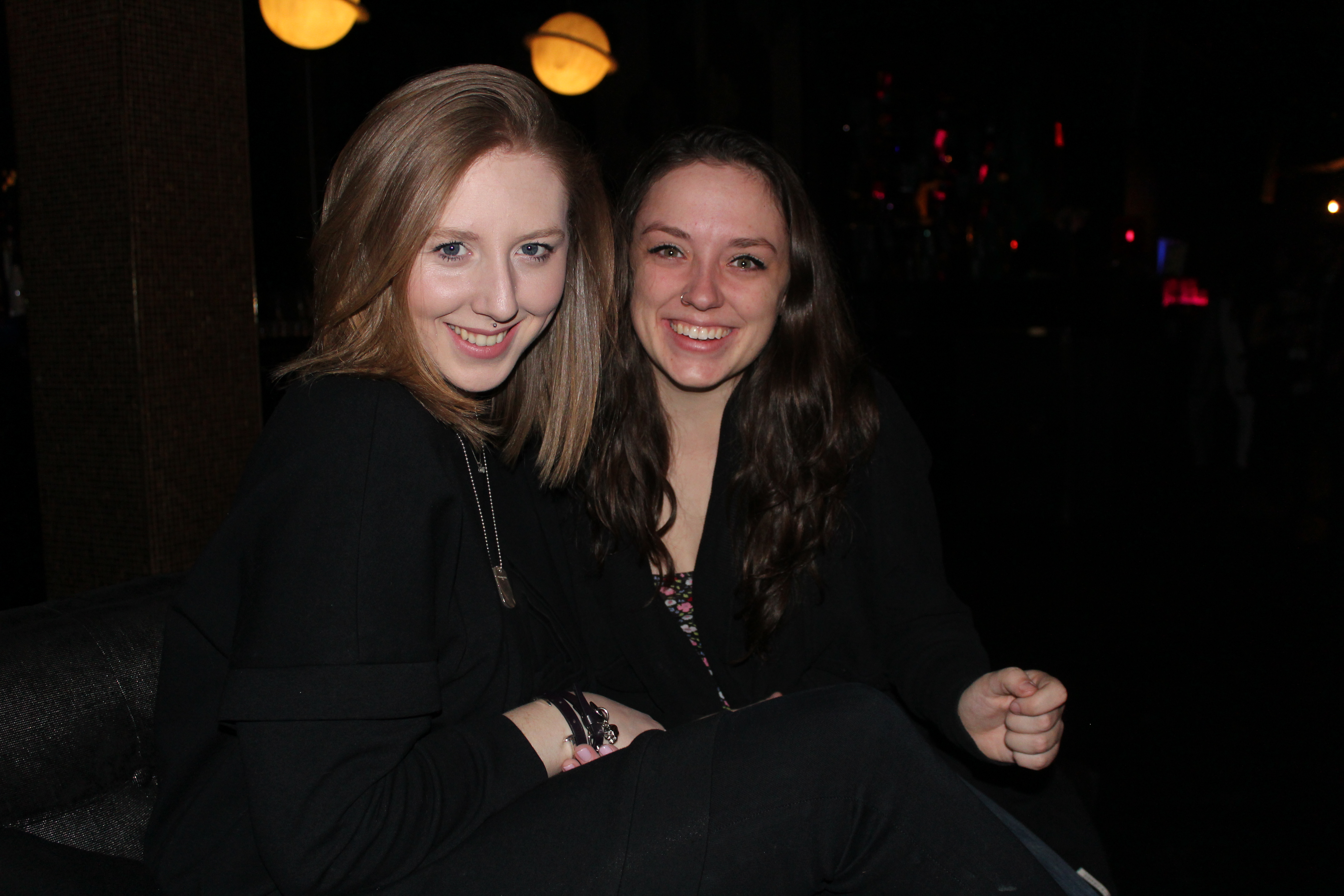 two university aged girls sitting on a large leather couch in a club-like setting