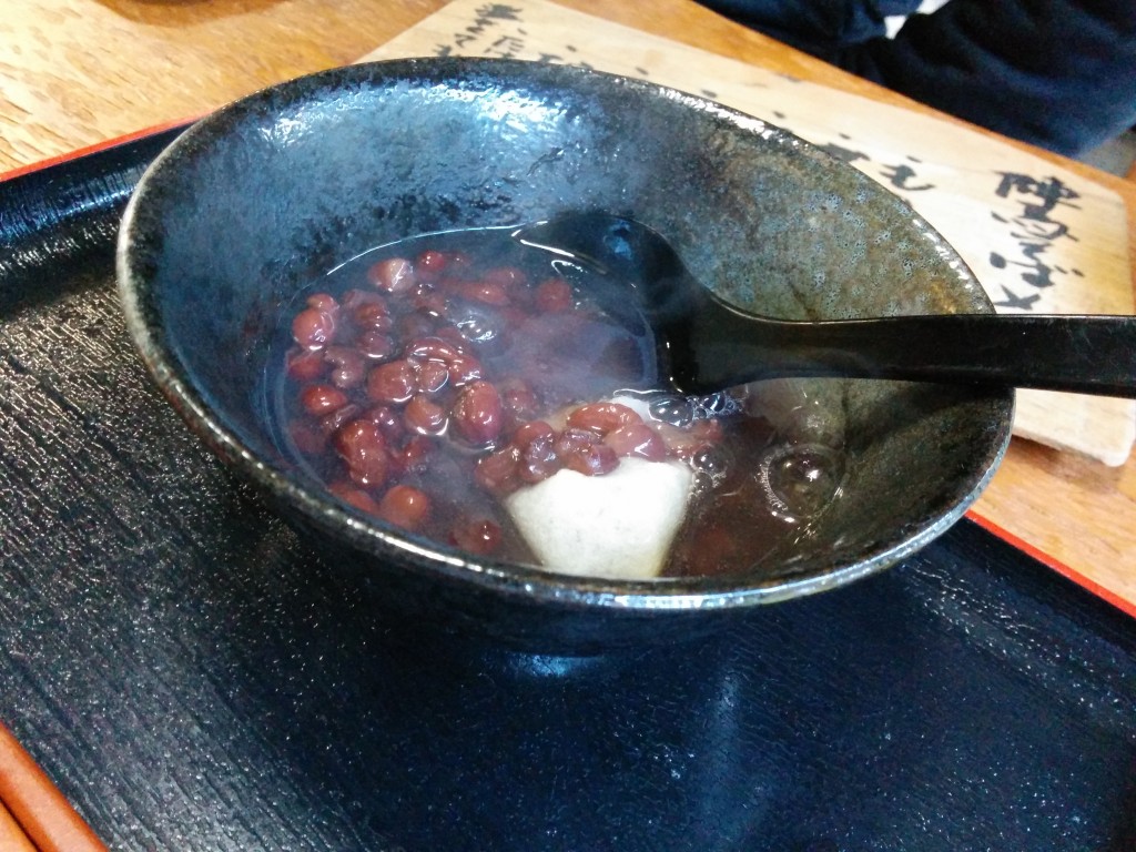 This image shows a steaming bowl of zenzai, red bean soup, with a piece of mochi, rice cake, inside.