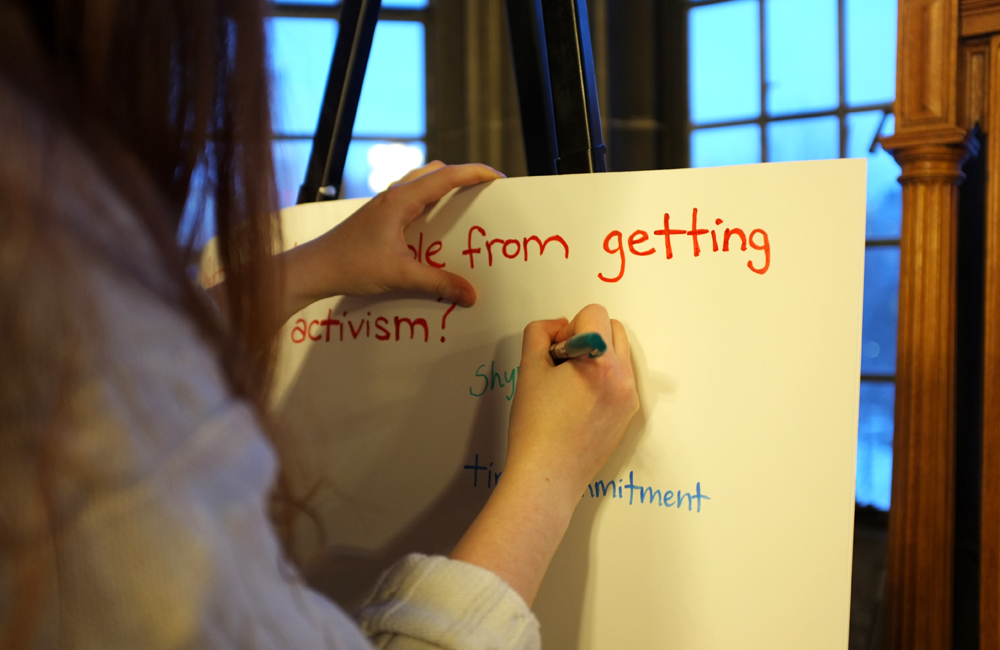 a person writes on a white bristol board to answer the question "what prevents you from getting involved in activism?" 