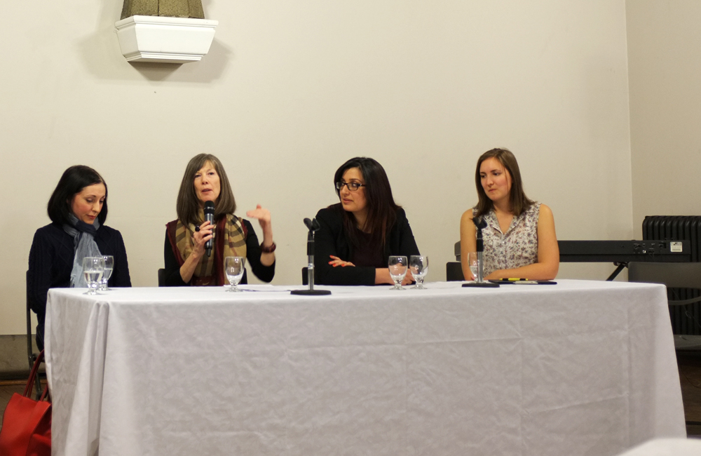 four women sit behind a table, one speaks into a microphone while the other three look on