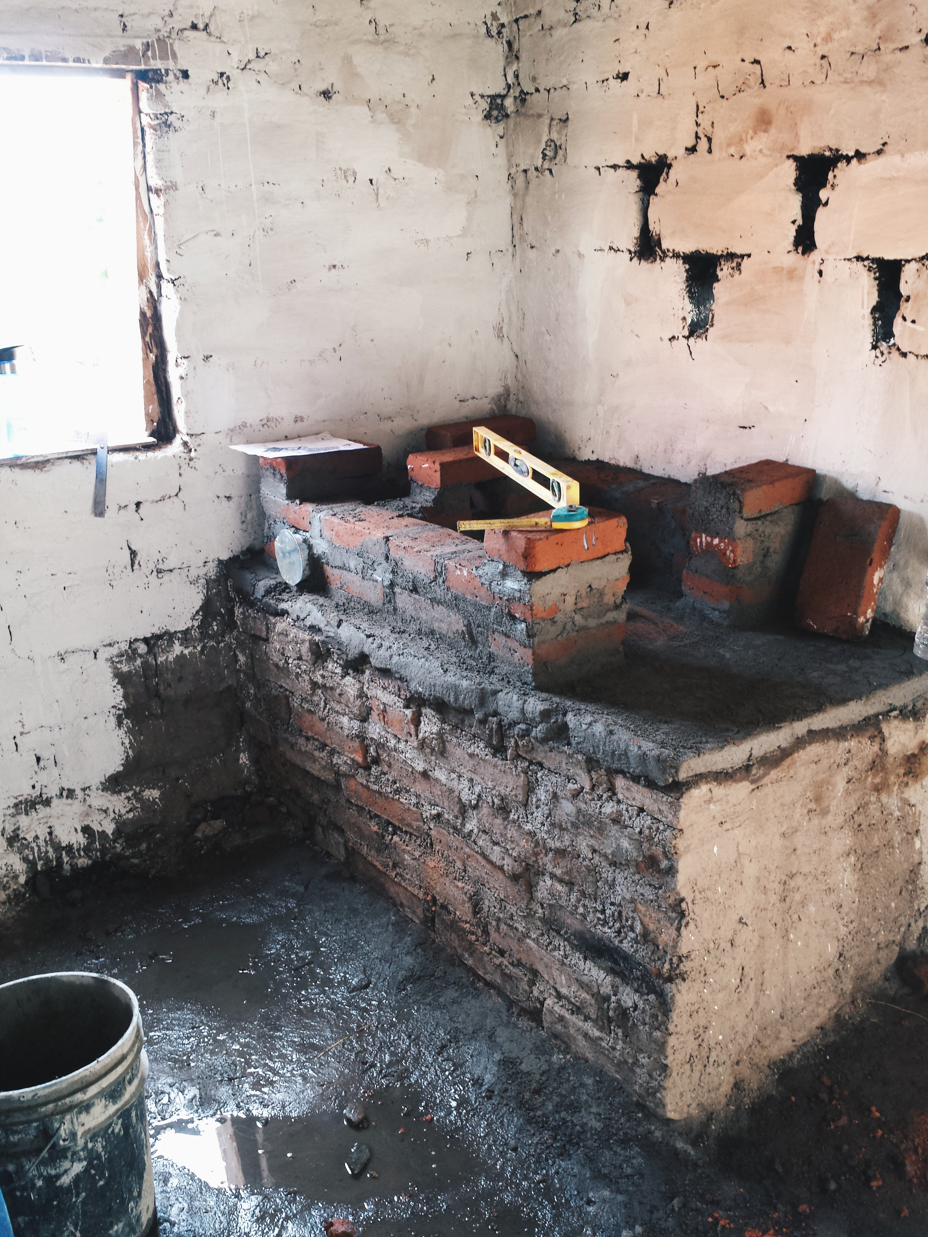 An outside room. In the corner of the room is a rectangular containment made of cement and bricks, which forms the base of the eco-stove.