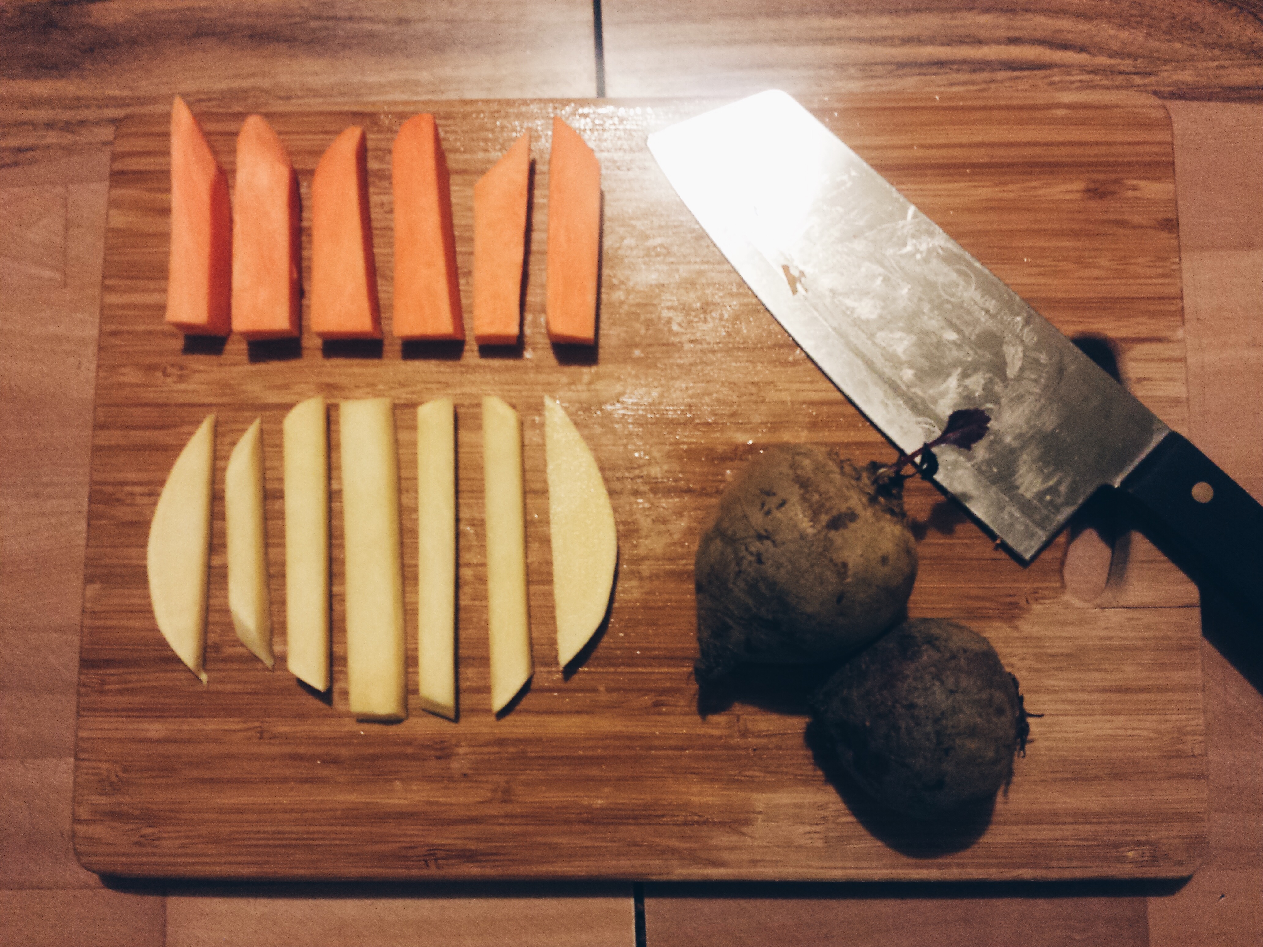 A cutting board with a knife, two whole beets, and sliced sweet potato and rutabaga.