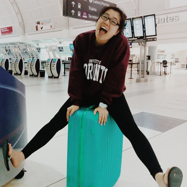 Kana sitting on a suitcase at the airport wearing her UofT sweater!
