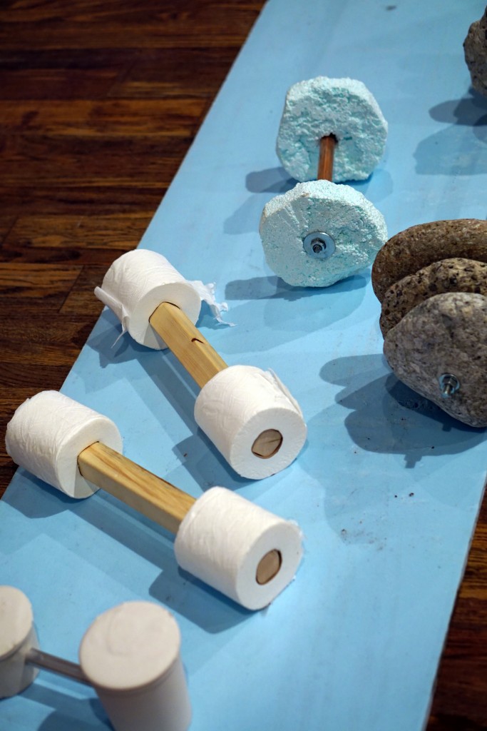 various barbell like sculptures, some of which have toilet paper rolls on each end instead of weights 