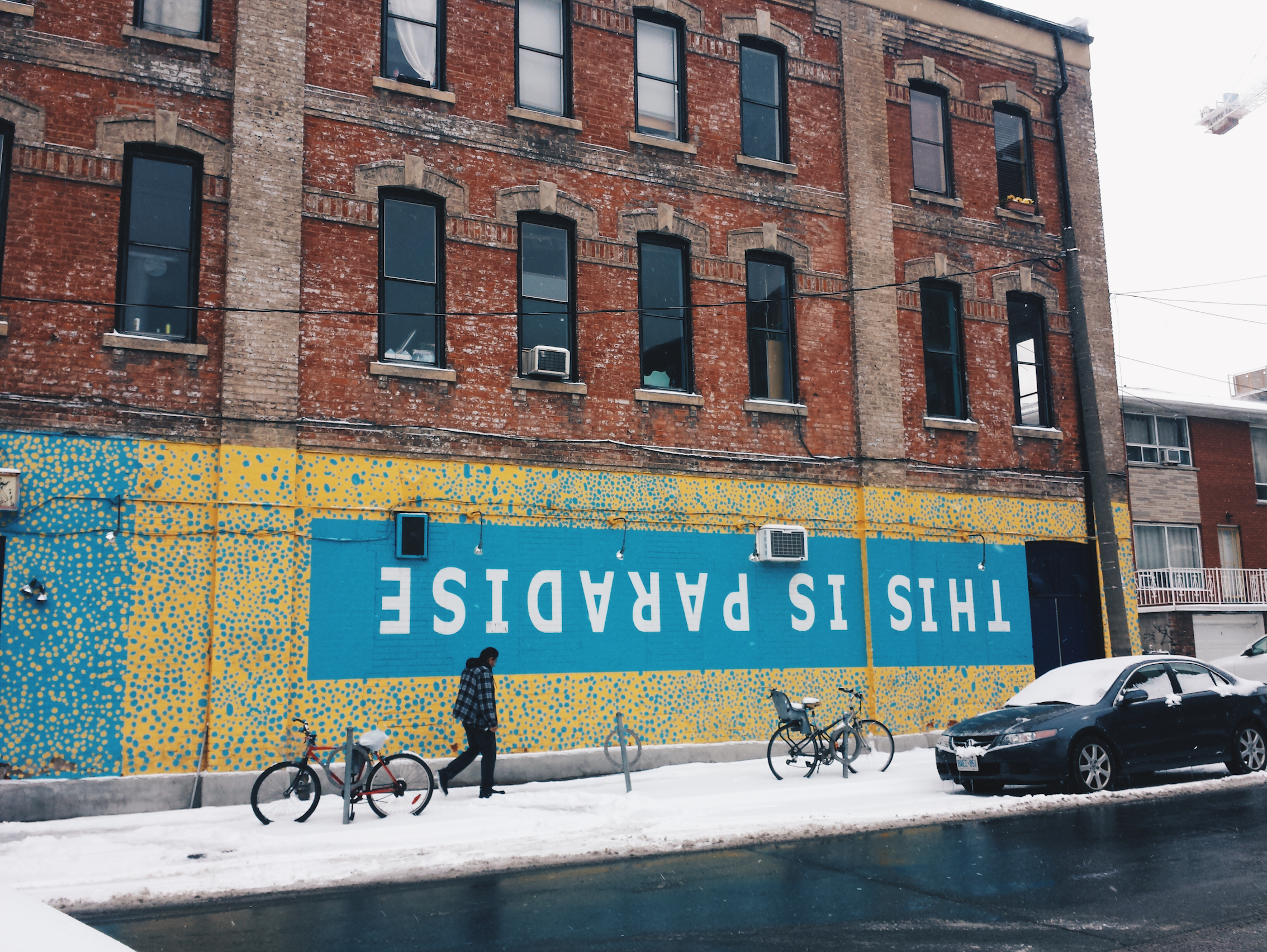 A mural on the side of a building saying "This is paradise." The ground is covered in snow and the sky is particularly grey and bleak