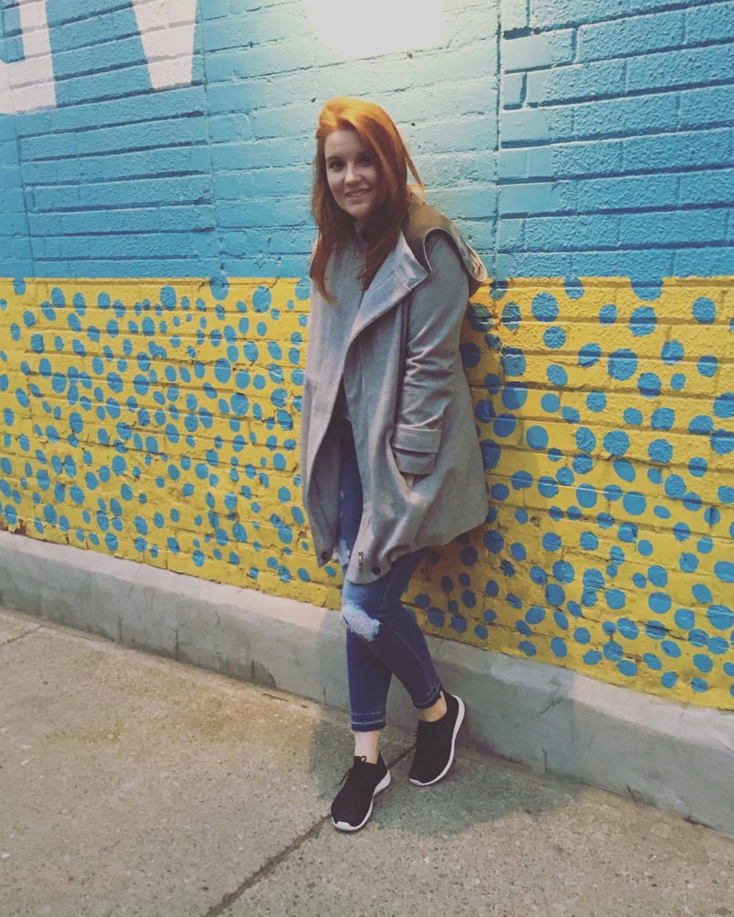 Madeline posing beside some street art. Graffiti that is blue and yellow polkadots on a brick wall.