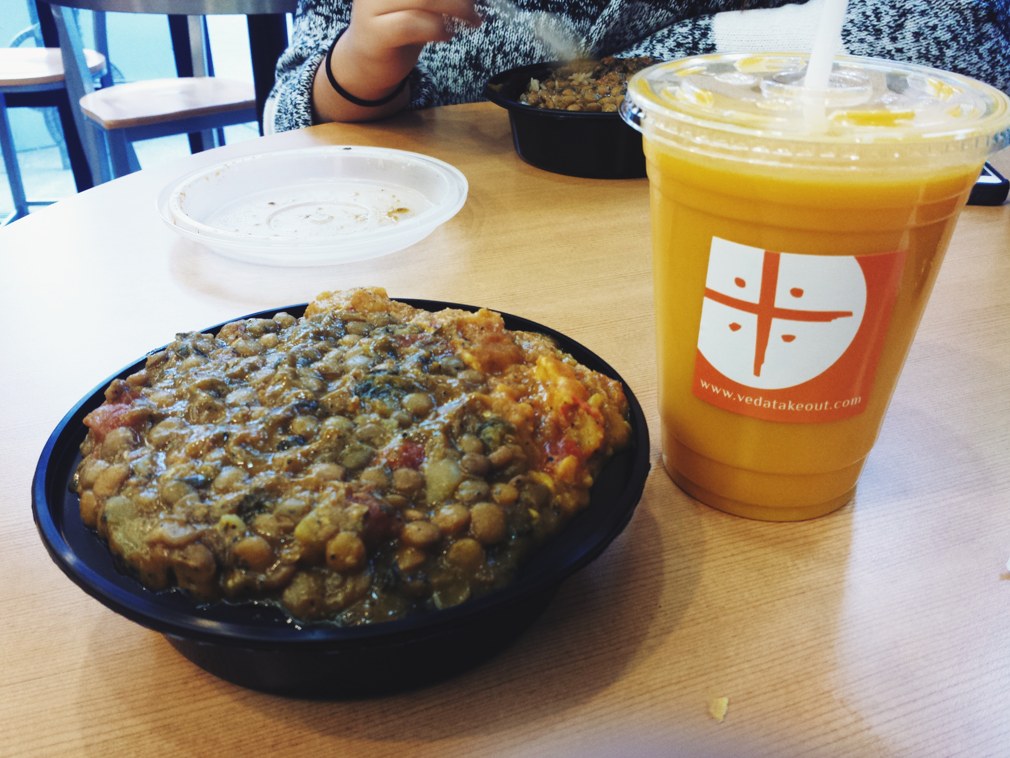 A container of curried lentils over rice and a cup of mango lassi.